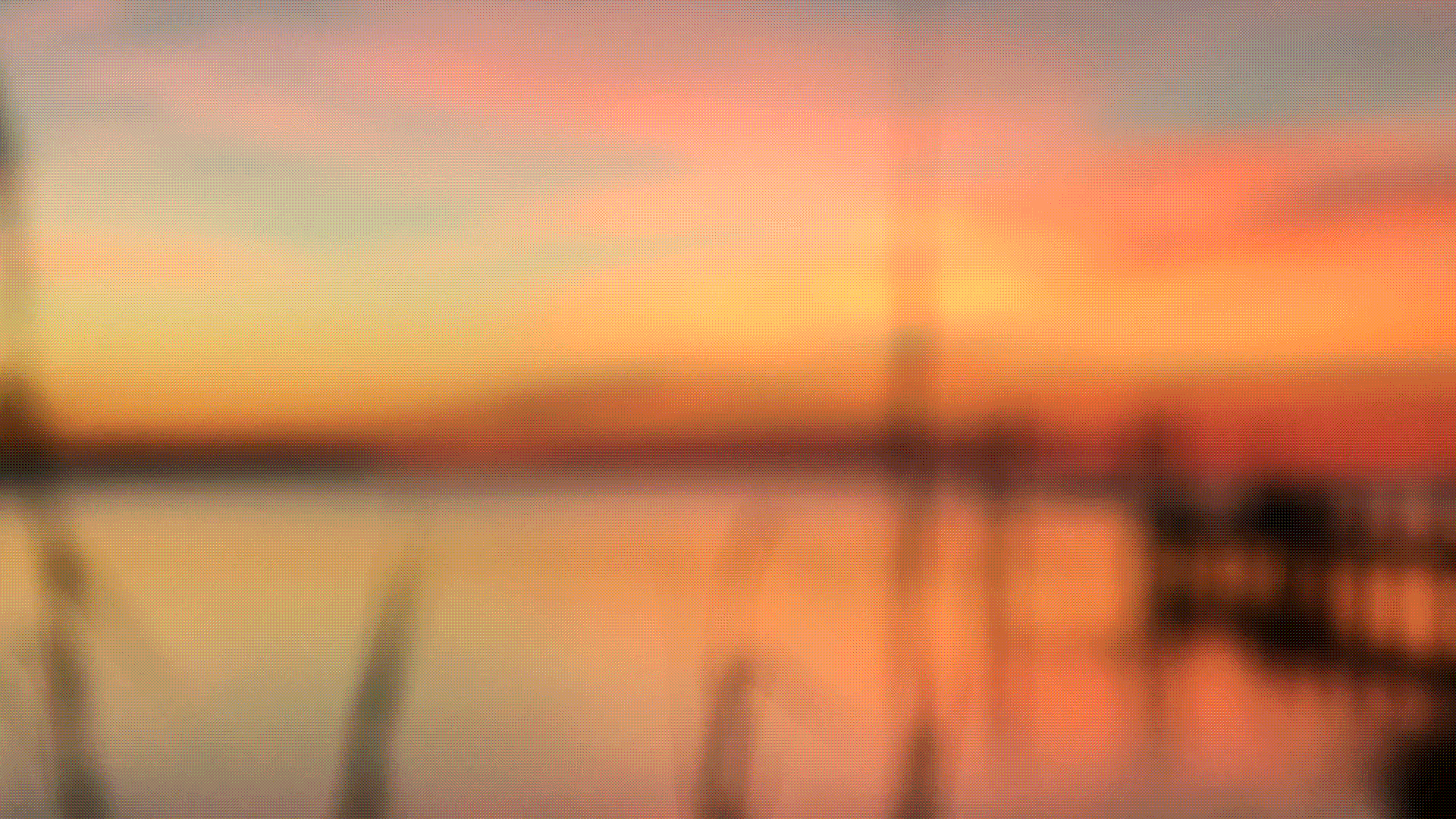 a blurred image of a brilliant sunset over a still sound, there's reeds in the foreground, a pier in the background, both in silhouette